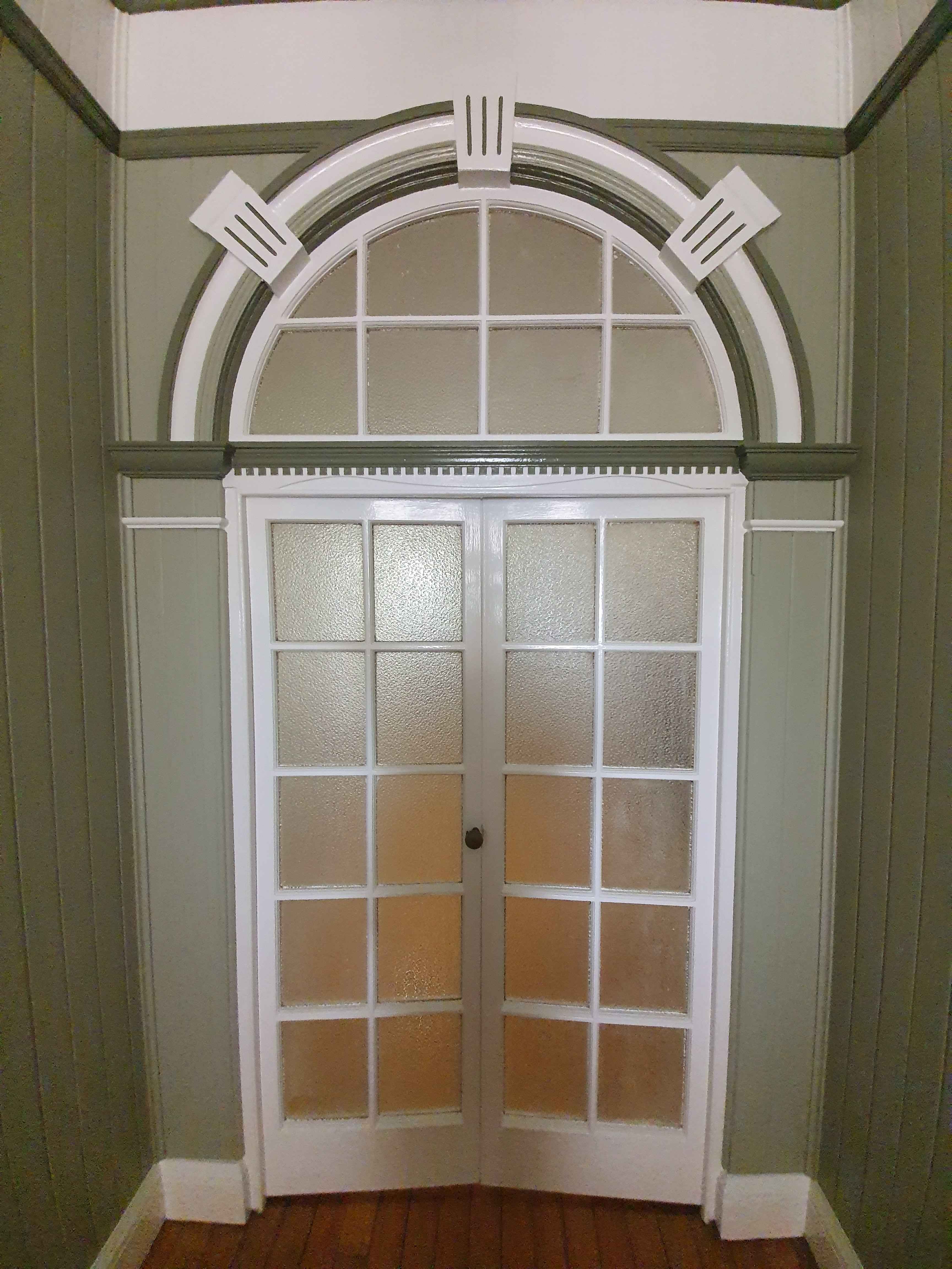 White French doors with multiple frosted glass panels, beneath a large arched transom window framed by decorative white trim.