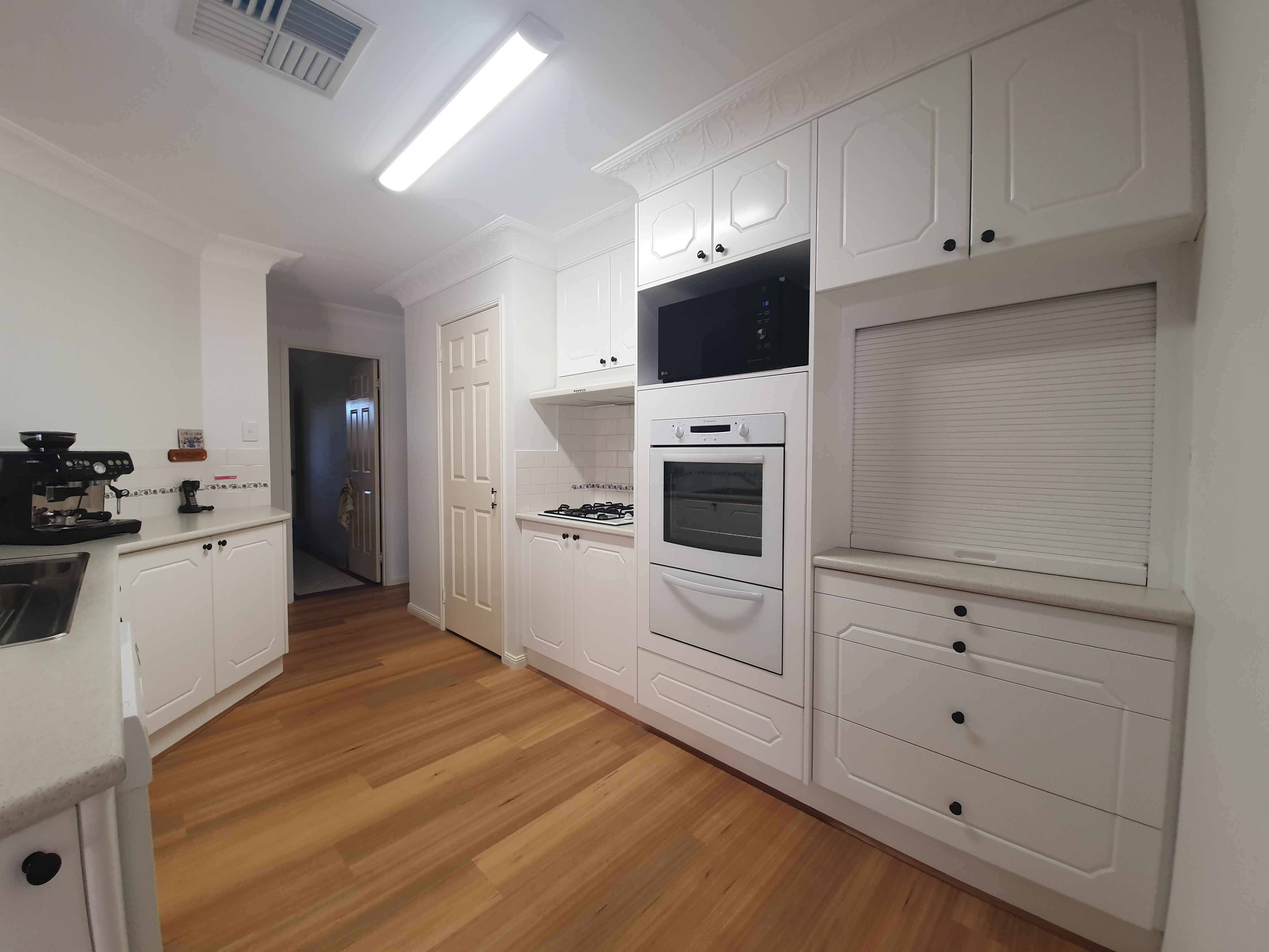 Bright white kitchen with tall cabinets, built-in microwave and double ovens, gas cooktop, and light wood floor